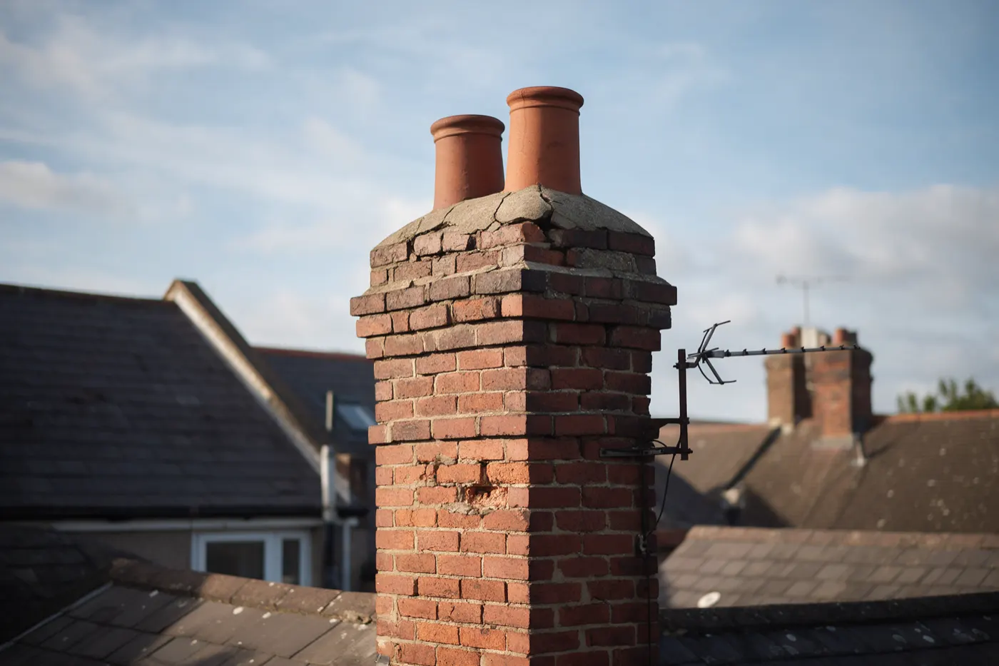 A brick chimney stack with crumbling mortar and cracked flaunching