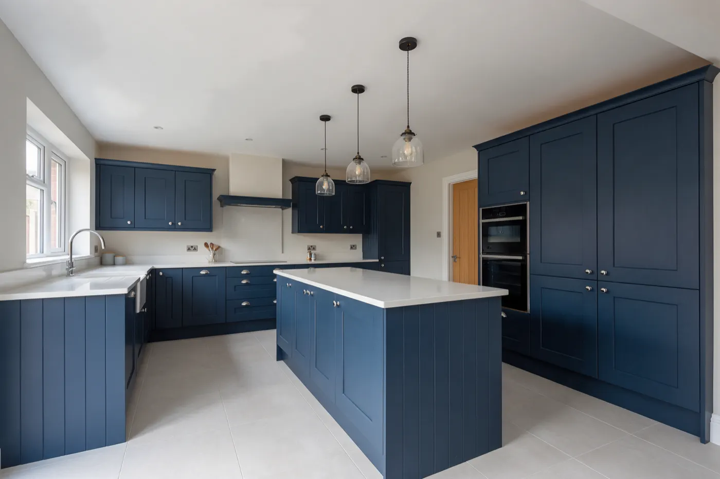 A finished kitchen with navy shaker units, an island and a pale stone worktop