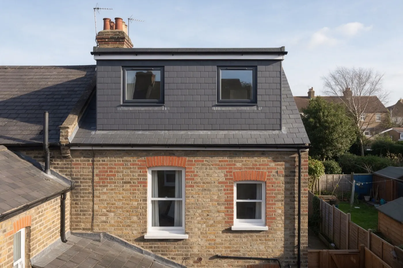 A box dormer loft conversion clad in grey slate on the back of a Victorian brick terraced house
