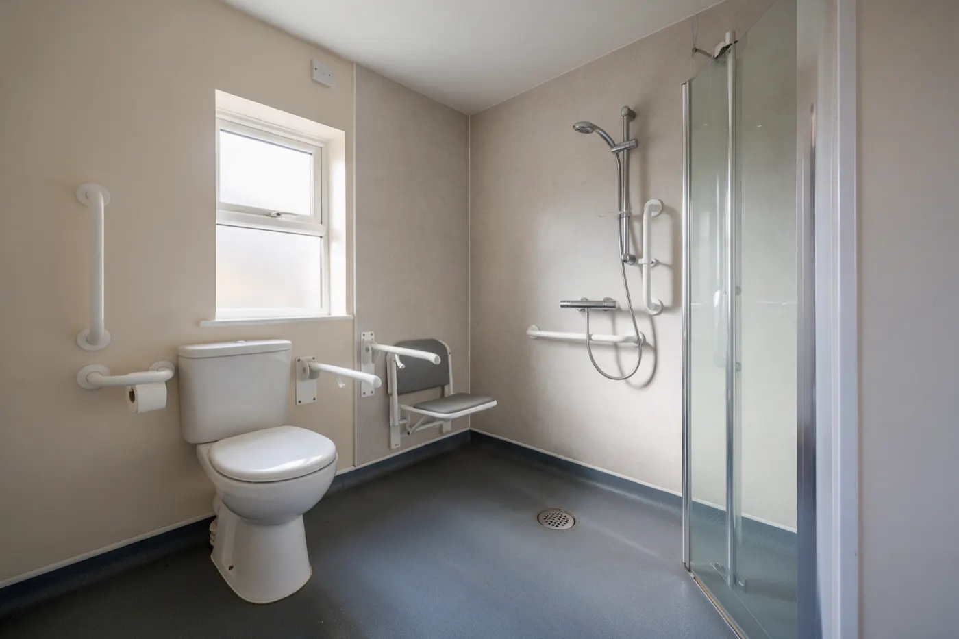 An accessible bathroom with a level-access shower, grab rails and a fold-down seat