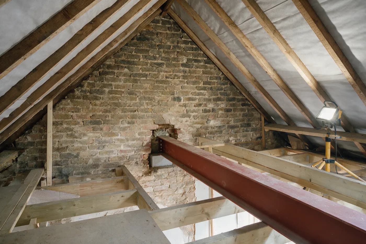 A loft conversion under way in a Victorian terrace: a red steel beam built into a pocket in the brick party wall, resting on a concrete padstone, with new timber floor joists alongside