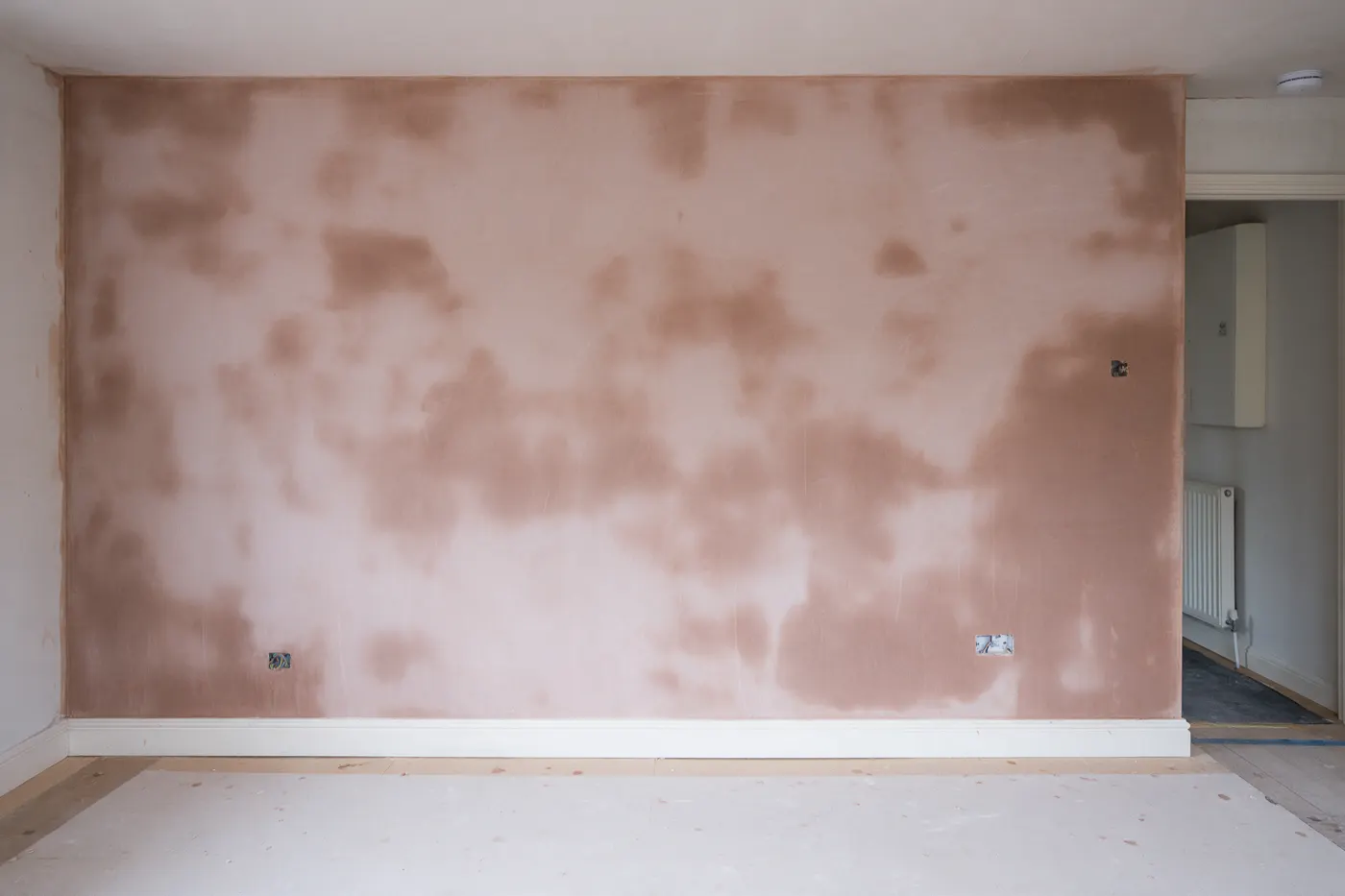 A freshly skimmed wall still drying, darker in patches